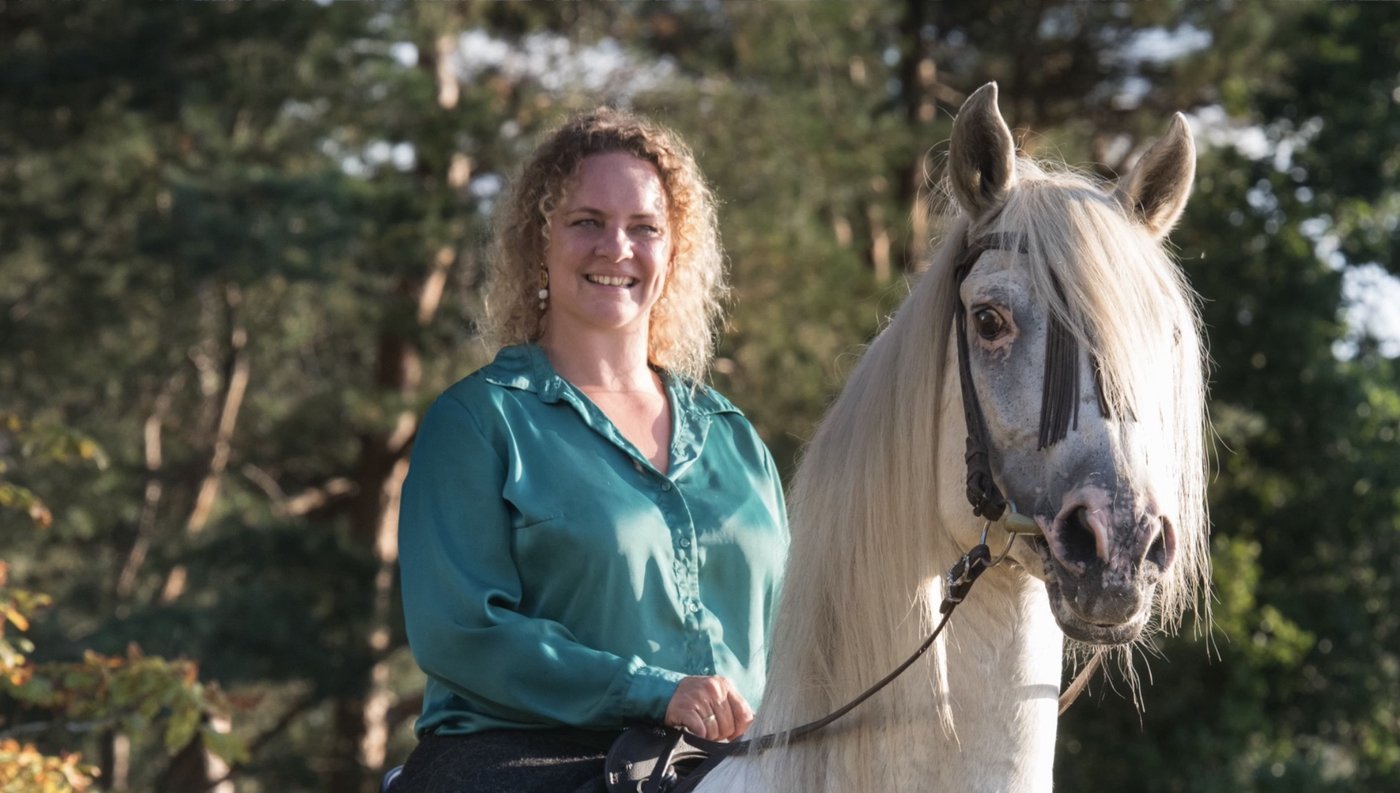 Miriam Thoma im grünen Hemd neben einem hellen Andalusier-Pferd im Abendlicht